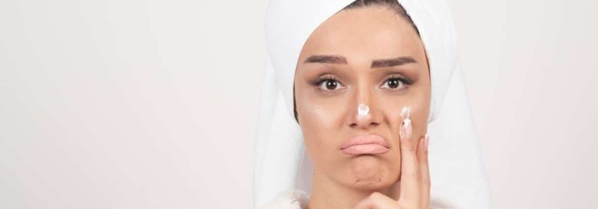Woman in a bathrobe applying cream of dull skin
