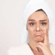 Woman in a bathrobe applying cream of dull skin