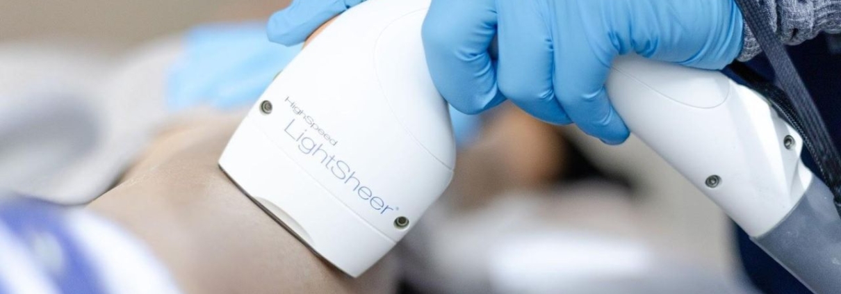 Laser hair removal device applied to a person’s leg by a technician wearing blue gloves in a clinical setting