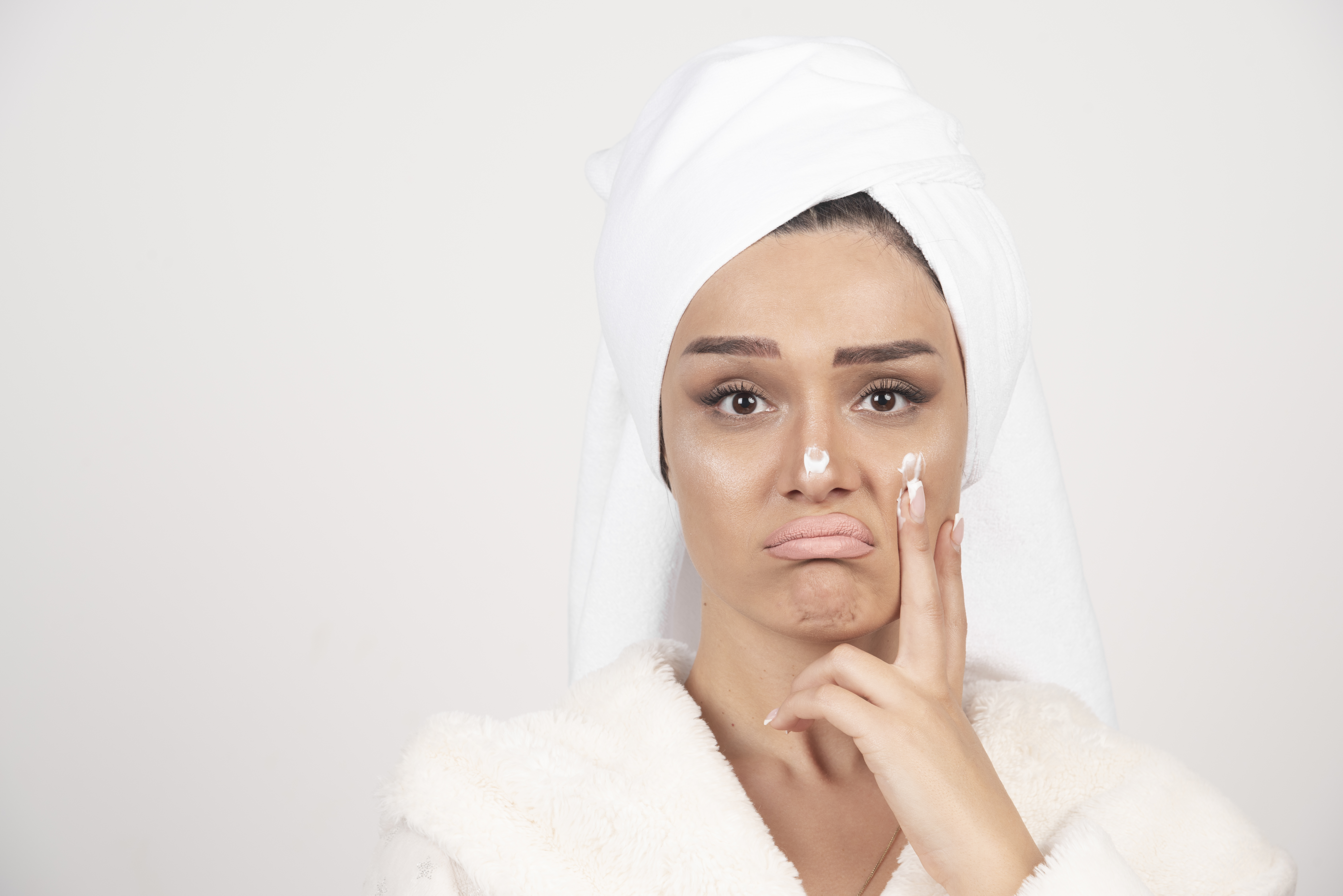 Beautiful young woman in a white bathrobe posing on a white wall
